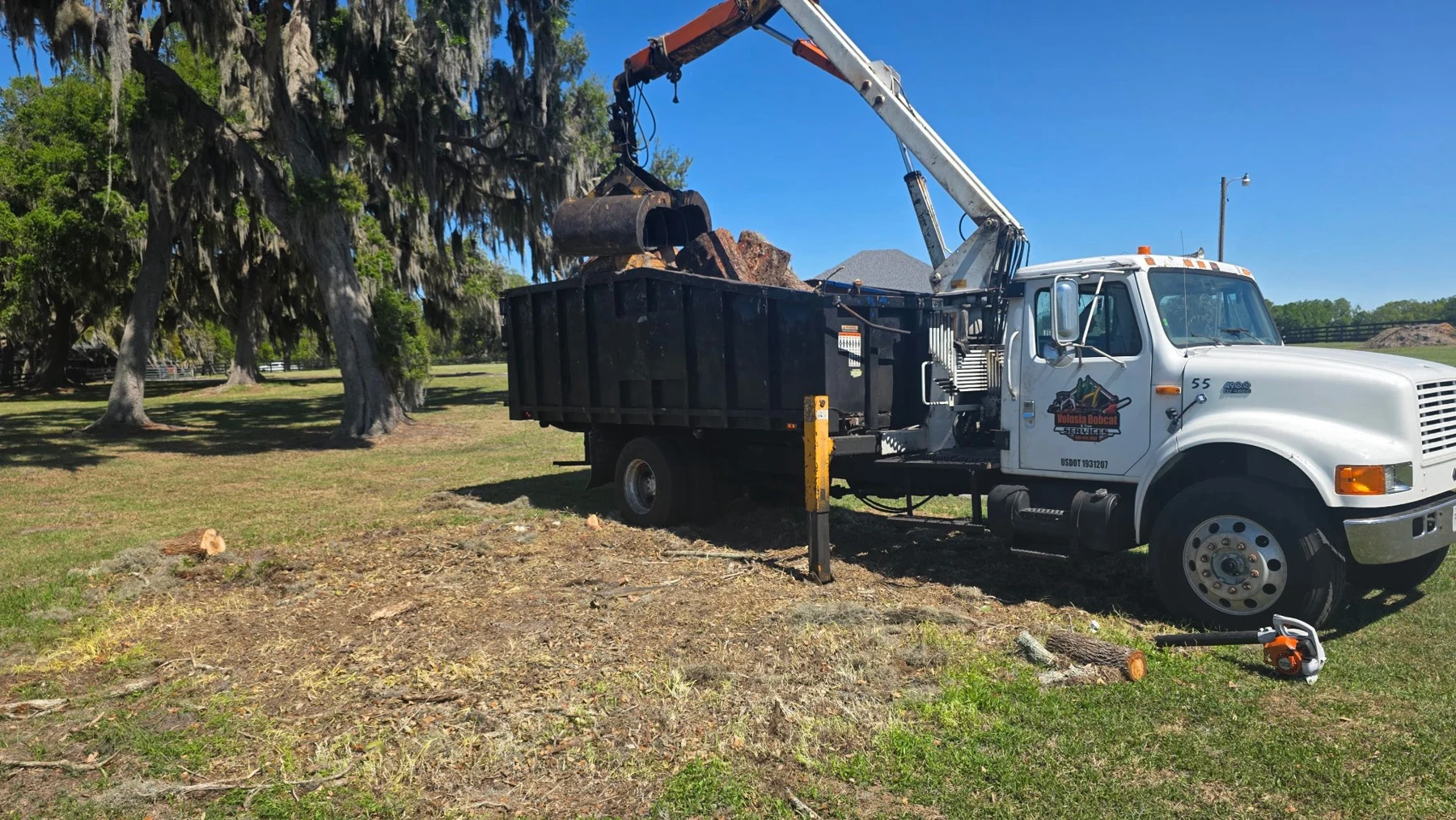 Grapple truck loading heavy debris and logs from a property