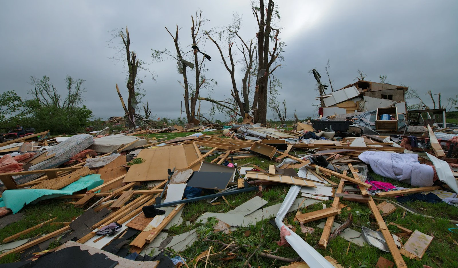 A large pile of storm debris on a green field awaiting removal