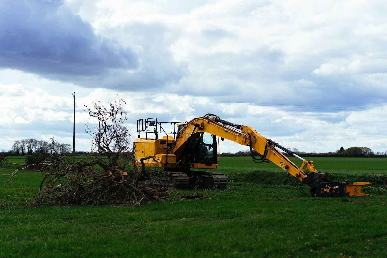 Yellow excavator clearing branches in a grassy field