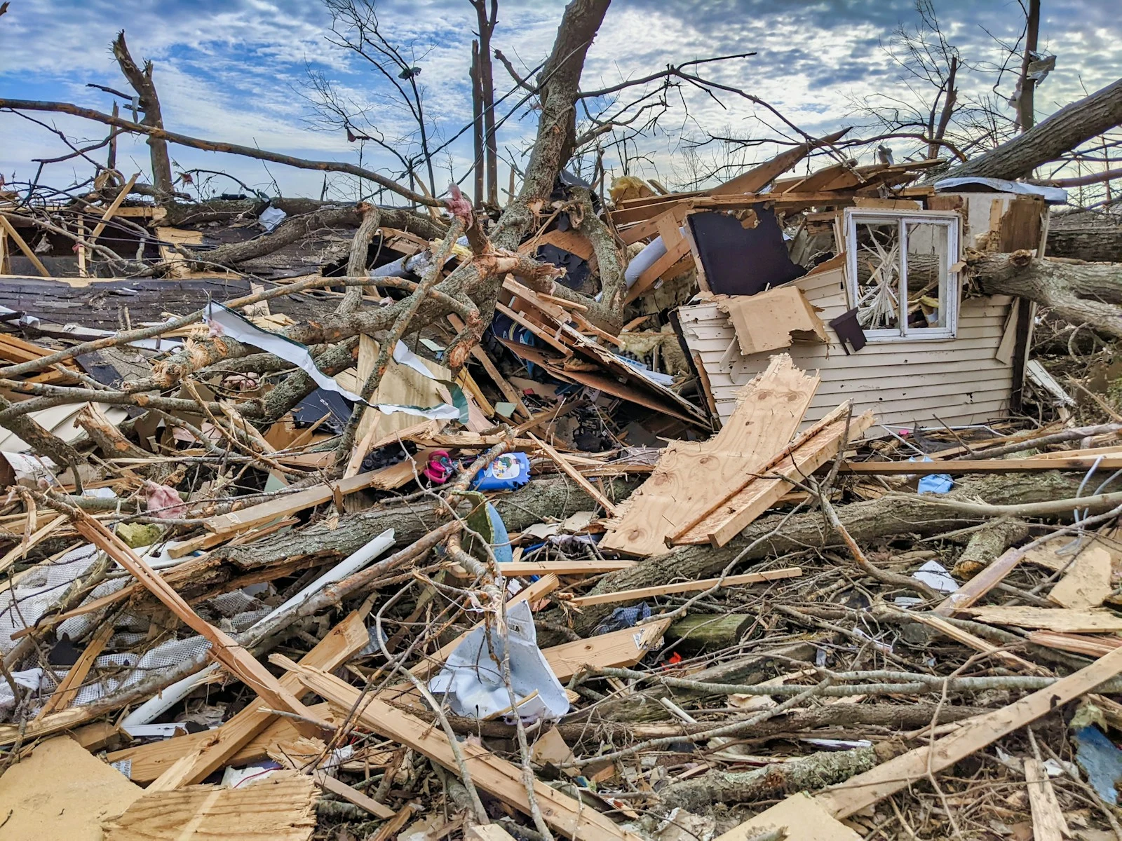Storm-damaged property with debris in front of a house